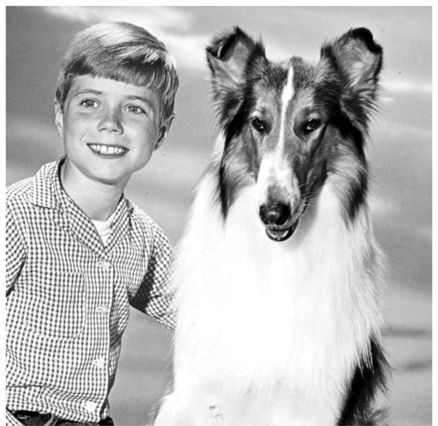 Young boy smiling beside a rough collie dog in a vintage black-and-white publicity photo