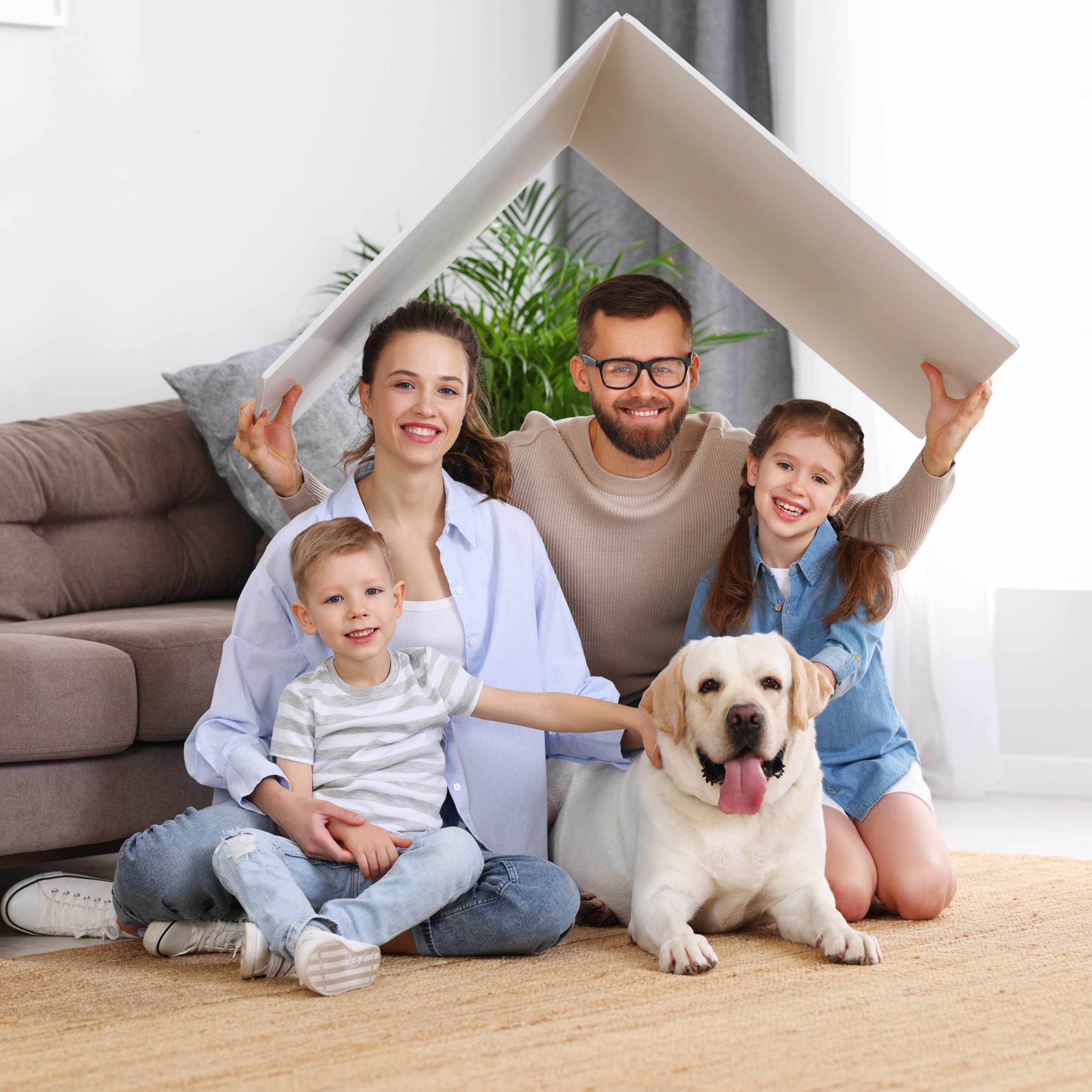 Family smiling with their Labrador in a living room under a makeshift cardboard roof