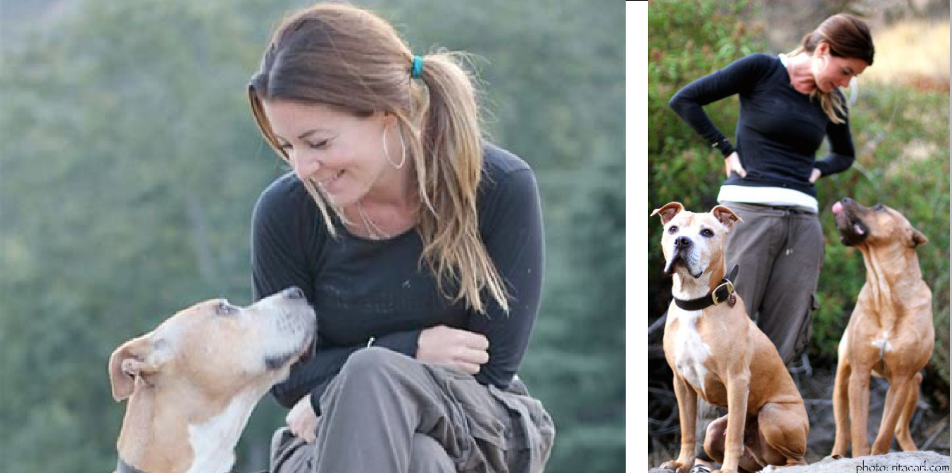 Woman kneeling and smiling at two tan dogs in a grassy outdoor setting