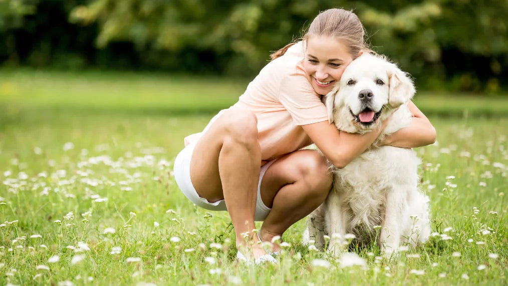 Woman crouching in a grassy field hugging a large white fluffy dog