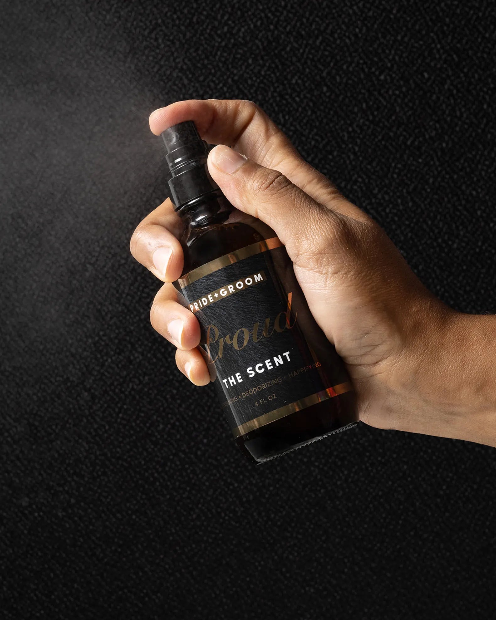 Close-up of Pride+Groom The Scent dog cologne bottle being sprayed, mist visible against textured black background